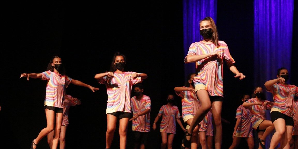 Alunas dançando em cima do palco vestindo uniformes coloridos.