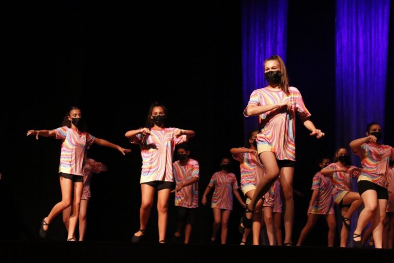 Alunas dançando em cima do palco vestindo uniformes coloridos.