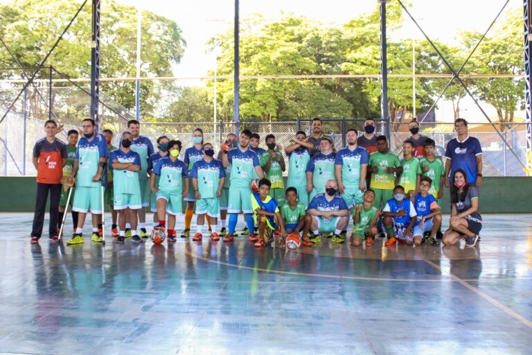 Alunos dos projetos Vem Ser e Bola Bacana Ribeirão reunidos vestindo uniformes verdes e azuis e posando para a foto.