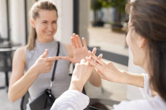Duas mulheres brancas de frente uma para a outra fazendo sinais em Libras.