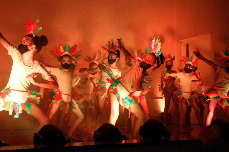 Alunas do projeto Amplié dançando em espetáculo com figurinos que lembram a cultura indígena.